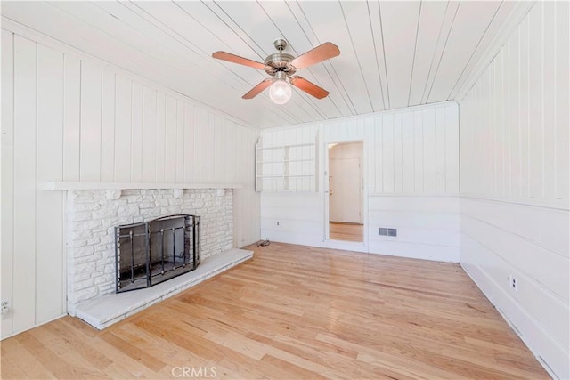 unfurnished living room with a fireplace with raised hearth, wood finished floors, ceiling fan, wooden ceiling, and wood walls