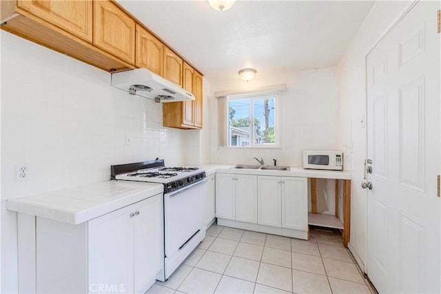 kitchen featuring under cabinet range hood, white appliances, a sink, tasteful backsplash, and light tile patterned floors