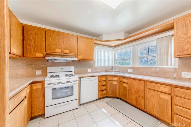 kitchen with white appliances, under cabinet range hood, a sink, light countertops, and light tile patterned flooring