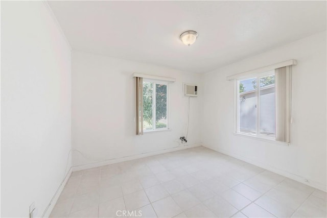 unfurnished room featuring plenty of natural light, an AC wall unit, baseboards, and light tile patterned floors