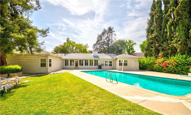rear view of property featuring a yard, a patio, an outdoor pool, and a chimney