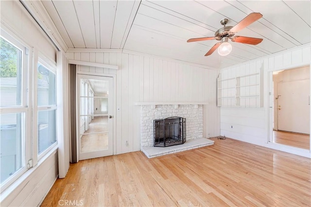 unfurnished living room with ceiling fan, wood finished floors, a brick fireplace, wood walls, and wooden ceiling