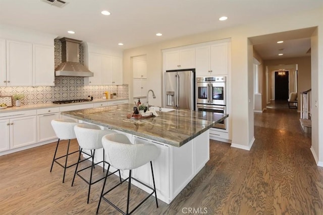 27086 Maple Tree Ct, Valencia, CA 91381 - kitchen with stainless steel appliances, wall chimney exhaust hood, wood finished floors, tasteful backsplash, and white cabinets