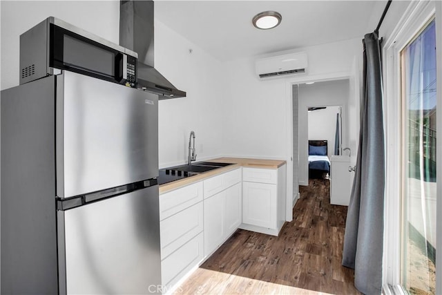 72473 Desert Trail Dr Unit 29, Palms, CA 92277 - kitchen with stainless steel appliances, a wall mounted air conditioner, wall chimney range hood, wood finished floors, and white cabinets