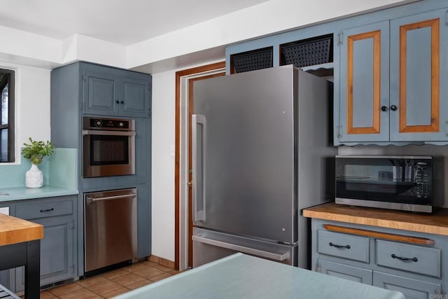 kitchen with stainless steel appliances, light tile patterned flooring, and butcher block countertops