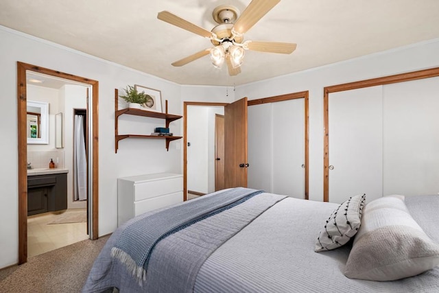 bedroom with two closets, light colored carpet, connected bathroom, ceiling fan, and ornamental molding