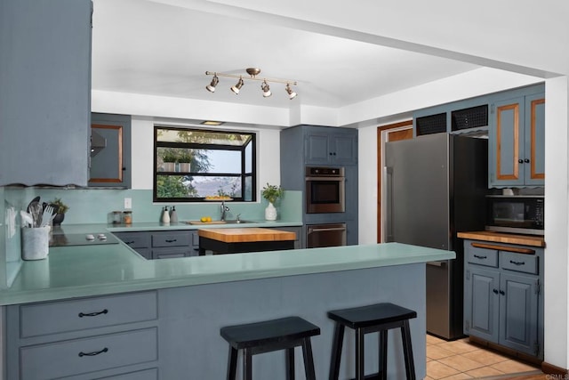 kitchen with appliances with stainless steel finishes, a sink, a peninsula, light tile patterned floors, and a breakfast bar area