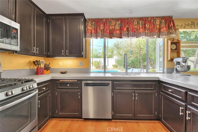 6730 Harrington Ct, Chino, CA 91710 - kitchen with appliances with stainless steel finishes, a sink, light countertops, light wood-style floors, and dark brown cabinets