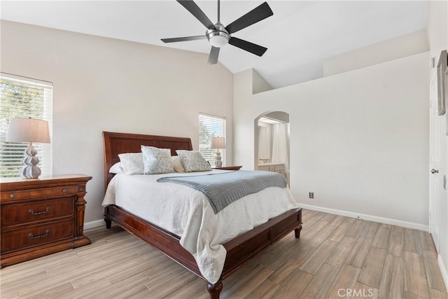 bedroom with arched walkways, multiple windows, light wood-style flooring, and high vaulted ceiling