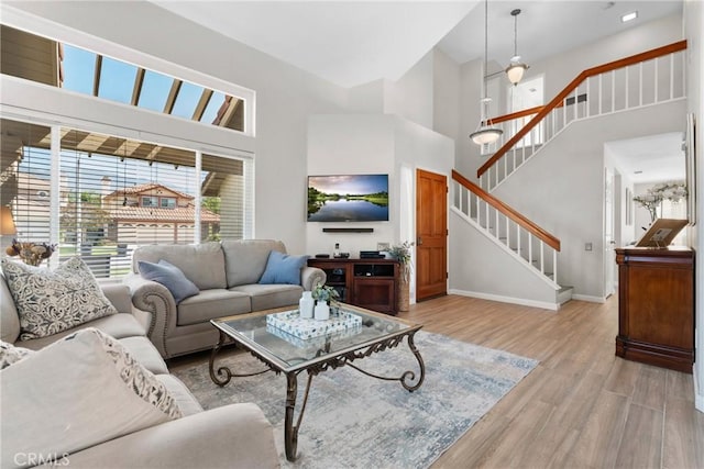 living room with a high ceiling, stairway, light wood-style floors, and baseboards