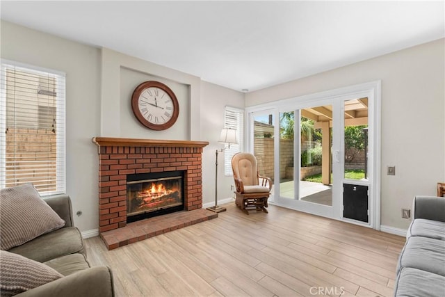 living area featuring light wood finished floors, a brick fireplace, and baseboards