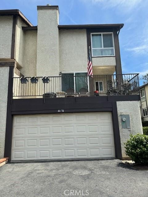 4676 Maxwell Ct, Riverside, CA 92501 - rear view of house featuring an attached garage, stucco siding, a balcony, a chimney, and concrete driveway