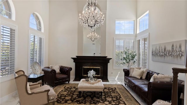 living room featuring a towering ceiling, a chandelier, baseboards, and a fireplace with flush hearth