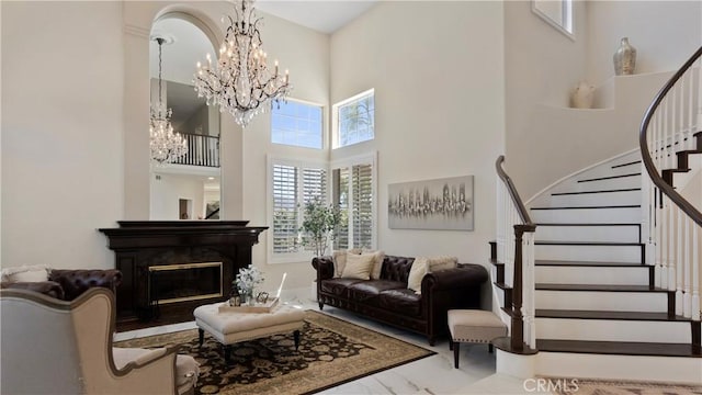 living room with a high ceiling, stairway, a chandelier, marble finish flooring, and a glass covered fireplace