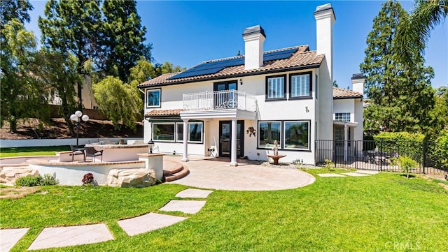 rear view of property featuring a balcony, a patio area, a chimney, and roof mounted solar panels
