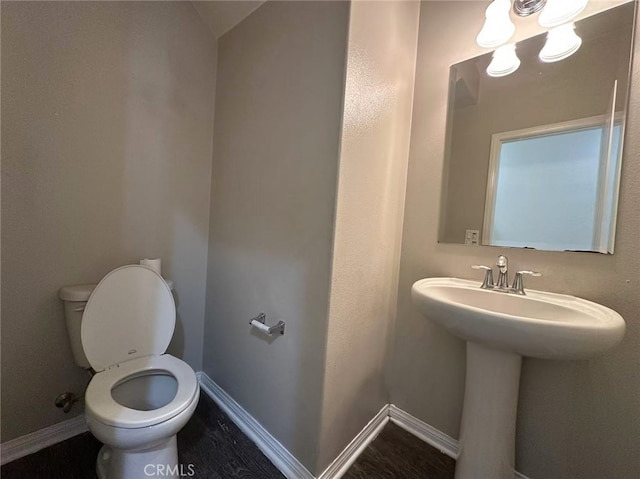 half bath featuring toilet, baseboards, and a sink