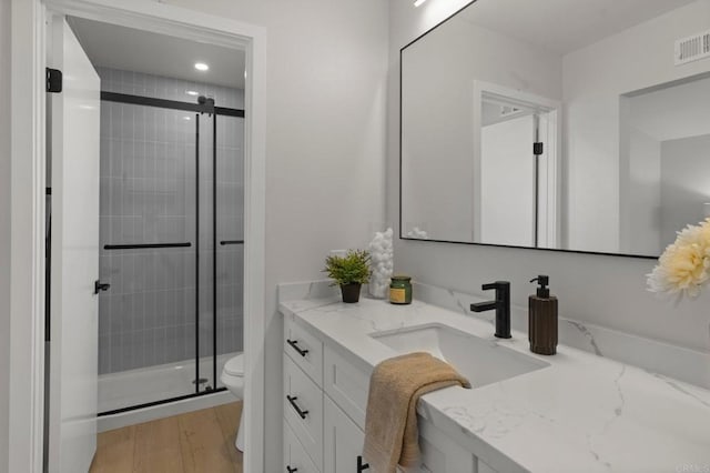 bathroom featuring a shower stall, toilet, vanity, wood finished floors, and recessed lighting