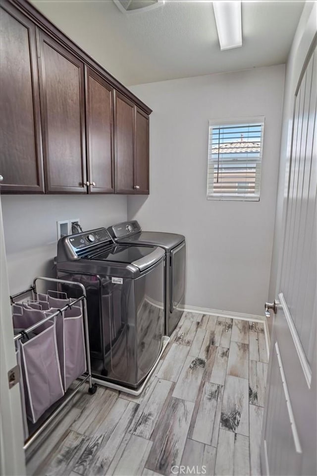 clothes washing area featuring independent washer and dryer, cabinet space, light wood-style floors, and baseboards