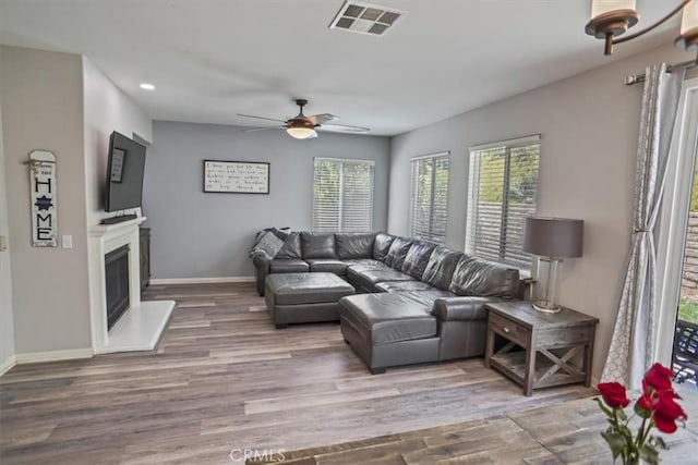 living room featuring wood finished floors, a ceiling fan, baseboards, a glass covered fireplace, and recessed lighting