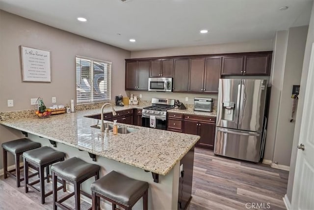 kitchen featuring appliances with stainless steel finishes, a sink, dark brown cabinets, light wood-style floors, and recessed lighting