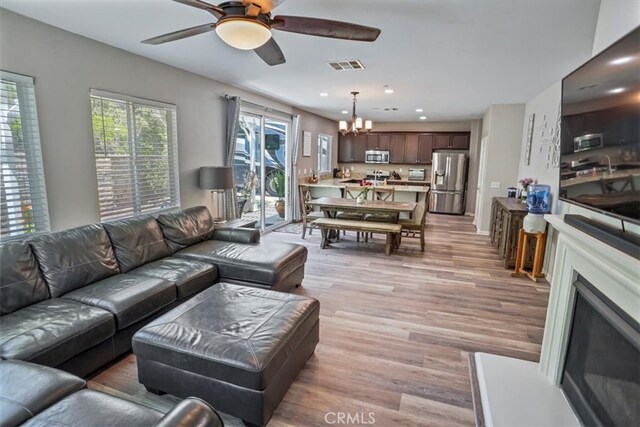 living room with a ceiling fan, a chandelier, light wood finished floors, recessed lighting, and a fireplace