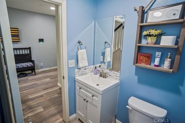 ensuite bathroom featuring toilet, wood finished floors, vanity, and baseboards
