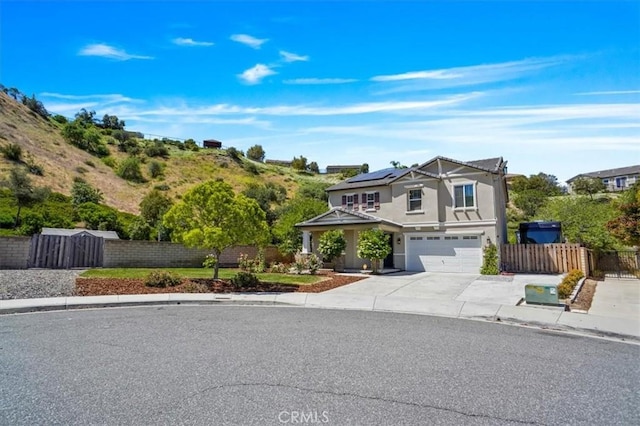 traditional-style house featuring roof mounted solar panels, a garage, fence, driveway, and stucco siding