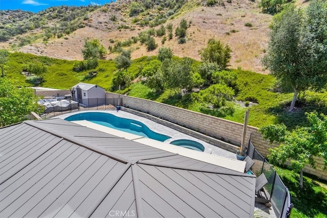 view of pool with an in-ground hot tub, a shed, a fenced backyard, an outbuilding, and a deck with mountain view