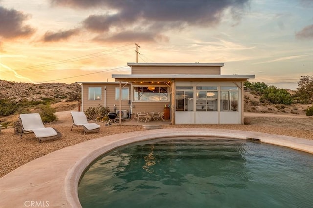 56714 Nelson Ave, Yucca Valley, CA 92284 - back of house at dusk with a sunroom, an outdoor pool, a patio, and curved driveway