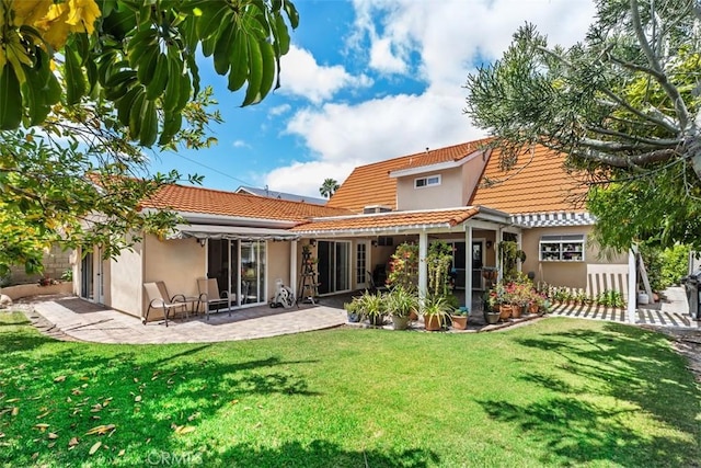 back of house featuring a tile roof, a patio area, a lawn, and stucco siding
