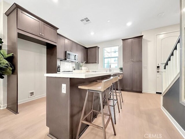 843 Cranberry Way, Upland, CA 91786 - kitchen featuring stainless steel microwave, light wood finished floors, dark brown cabinets, a kitchen island, and a breakfast bar area