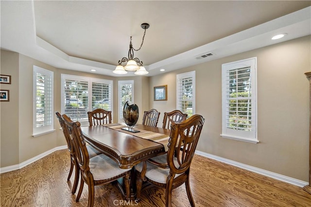 dining room featuring light wood finished floors, baseboards, a raised ceiling, plenty of natural light, and recessed lighting
