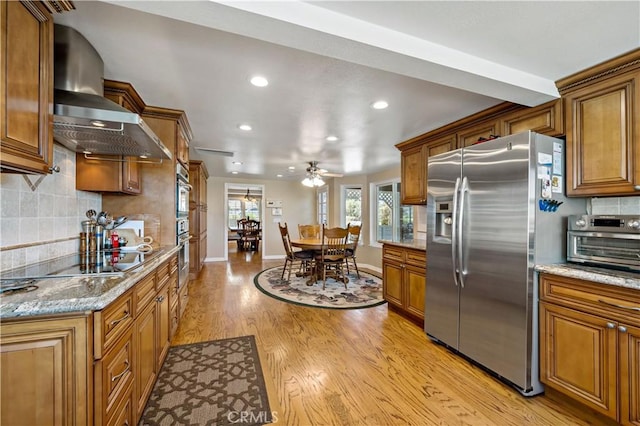 kitchen with stainless steel fridge, black electric stovetop, brown cabinetry, wall chimney exhaust hood, and recessed lighting
