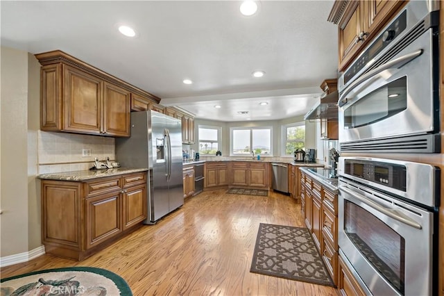 kitchen featuring appliances with stainless steel finishes, brown cabinetry, light wood-style floors, recessed lighting, and tasteful backsplash