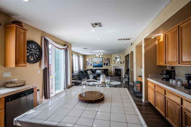 3035 Cat Tail Ct, Hemet, CA 92545 - kitchen with tile counters, stainless steel dishwasher, a tile fireplace, open floor plan, and recessed lighting