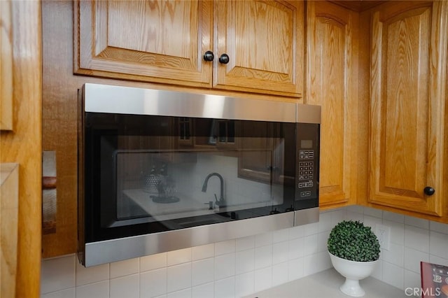 kitchen view of decorative backsplash, stainless steel microwave, brown cabinetry, and light countertops