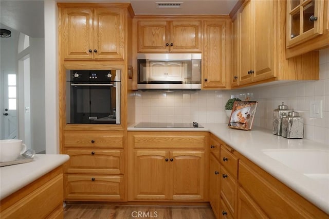 kitchen with stainless steel appliances, decorative backsplash, light countertops, and light wood-style flooring
