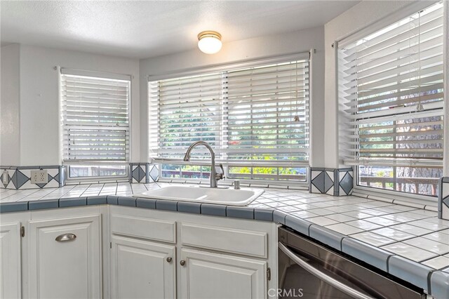 50711 Rd 426, Oakhurst, CA 93644 - kitchen featuring white cabinetry, stainless steel dishwasher, tile countertops, and a textured ceiling