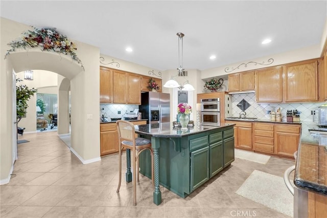43376 Terra Ct, Temecula, CA 92592 - kitchen featuring appliances with stainless steel finishes, backsplash, light tile patterned floors, a kitchen island, and arched walkways