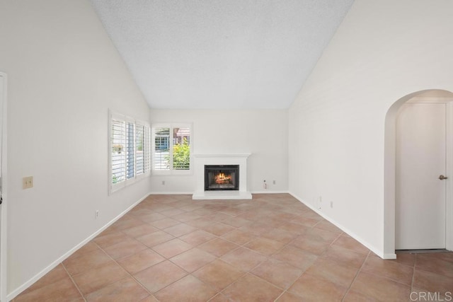 unfurnished living room featuring light tile patterned floors, a glass covered fireplace, arched walkways, high vaulted ceiling, and baseboards