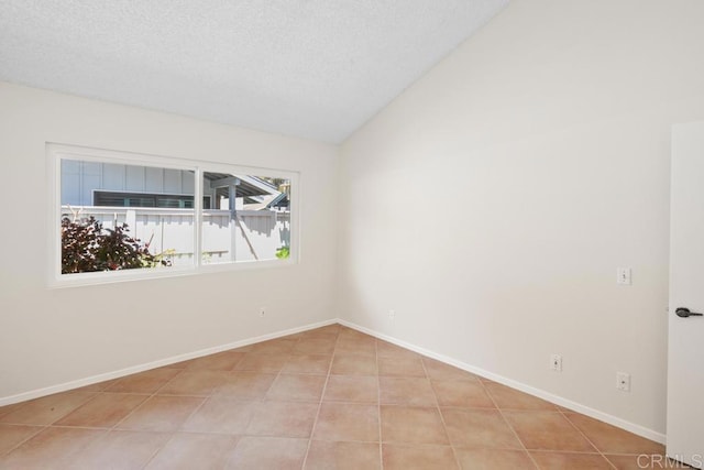 spare room with vaulted ceiling, a textured ceiling, tile patterned floors, and baseboards