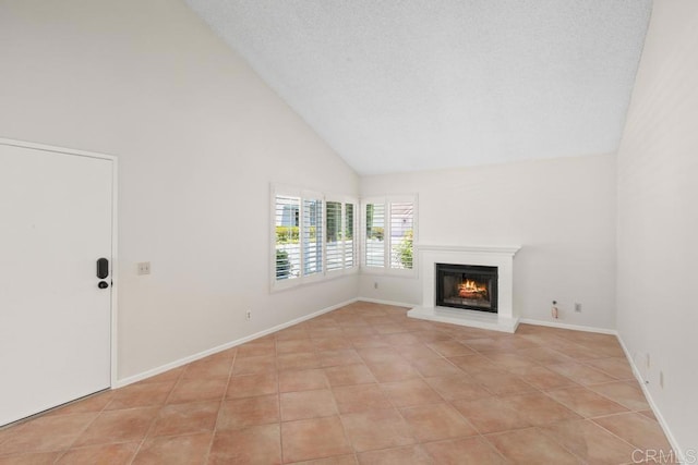 unfurnished living room with high vaulted ceiling, a glass covered fireplace, light tile patterned flooring, and baseboards