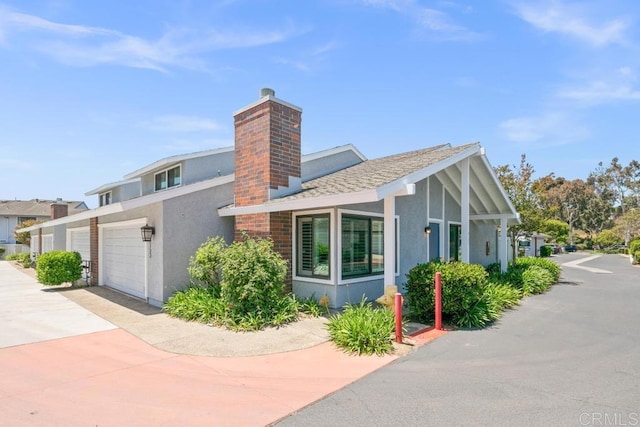 view of side of property featuring stucco siding, a chimney, concrete driveway, and an attached garage