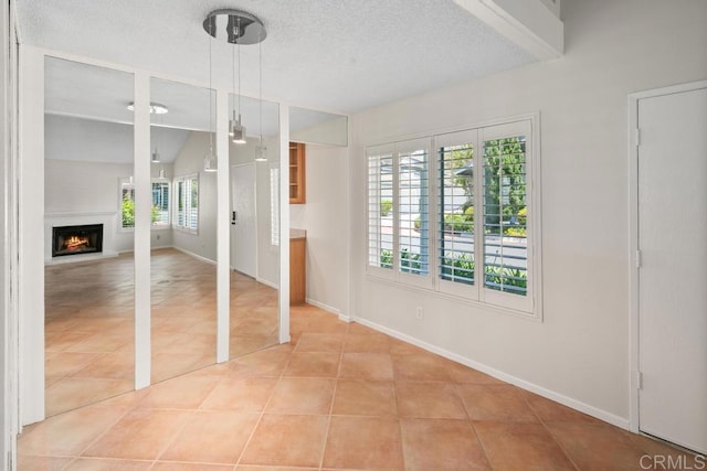 empty room featuring tile patterned floors, baseboards, a lit fireplace, a textured ceiling, and vaulted ceiling