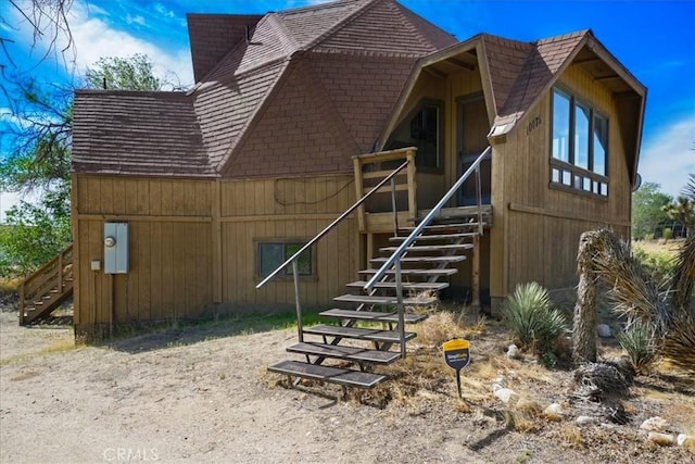 rear view of house featuring stairway and roof with shingles