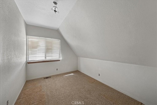 additional living space with vaulted ceiling, a textured ceiling, carpet flooring, and a textured wall