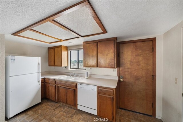 kitchen featuring white appliances, a sink, brown cabinets, a textured ceiling, and stone finish flooring