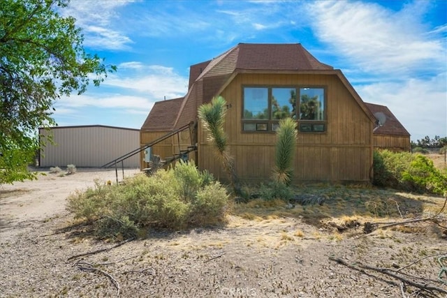 view of side of home featuring a shingled roof and an outbuilding