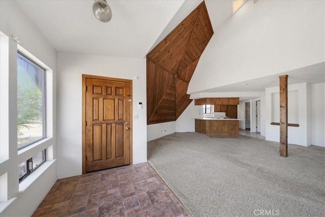 foyer entrance with healthy amount of natural light, high vaulted ceiling, and stone finish floors