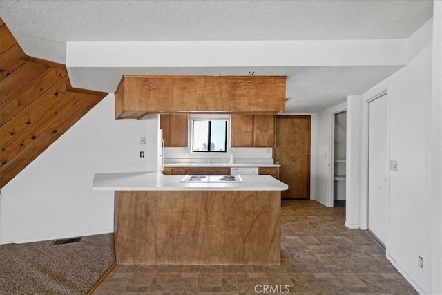 kitchen with brown cabinetry, a peninsula, light countertops, stone finish floors, and white electric stovetop